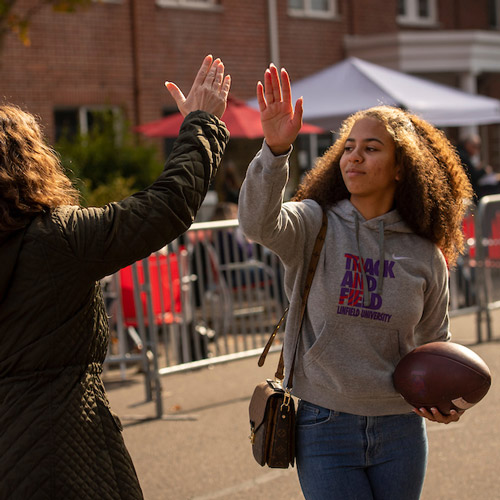 two students high-fiving on Streak Street before a football game