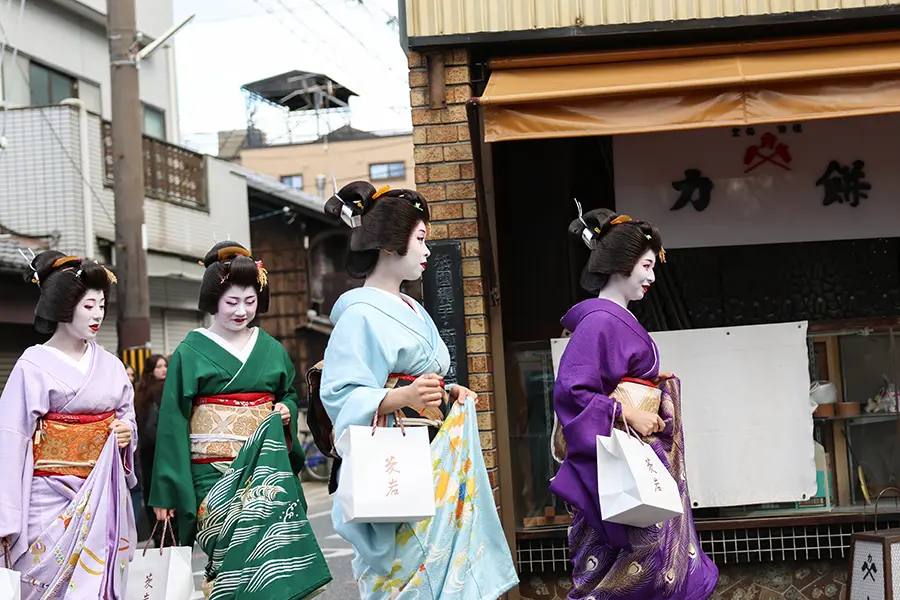 four maikos and giokos walk down a street.