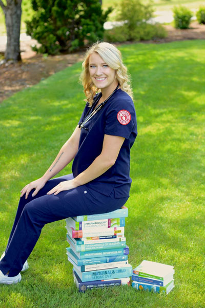 Kamryn in her nursing scrubs sitting on pile of books