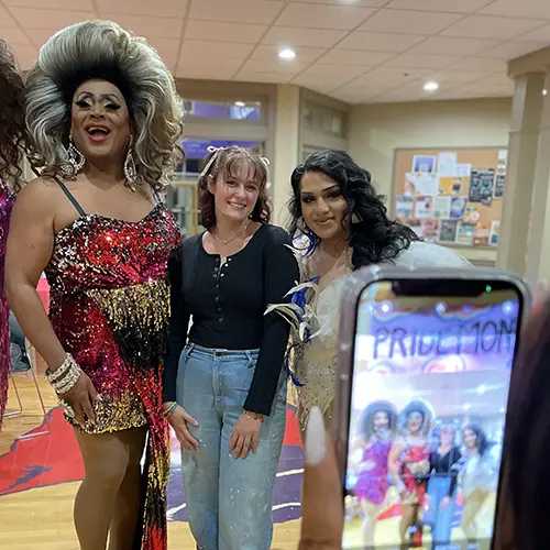 a drag queen posing with students for a photo at bingo night.