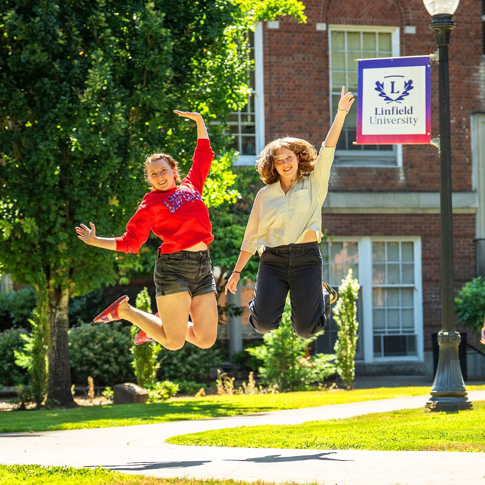 Students jumping in front of a Linfield banner.