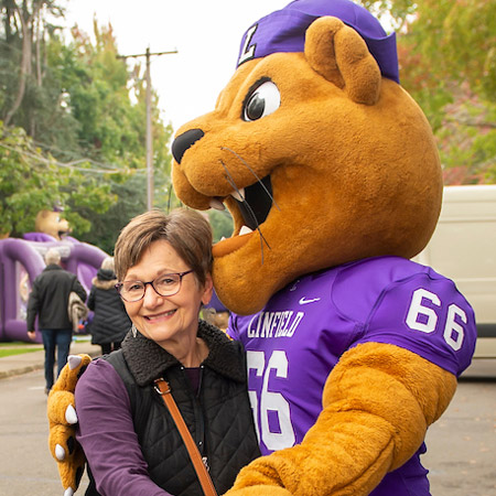 Mack the Wildcat hugging a Linfield alumnus at Homecoming 2023.