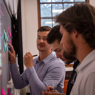 Three graduate students writing notes at the classroom whiteboard.