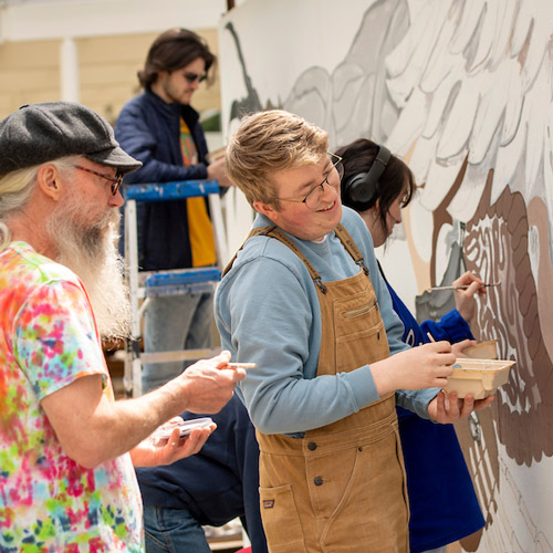 students painting a mural on the fine arts center with Professor Totem Shriver