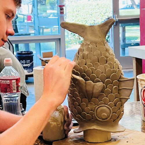 Student creating a ceramic piece of a fish