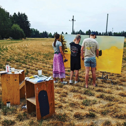 three students painting on easels outdoors