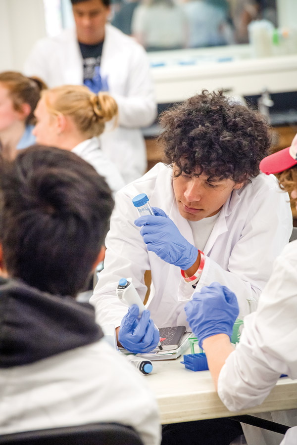 Three students at a table inspecting a sample specimen in a tube.