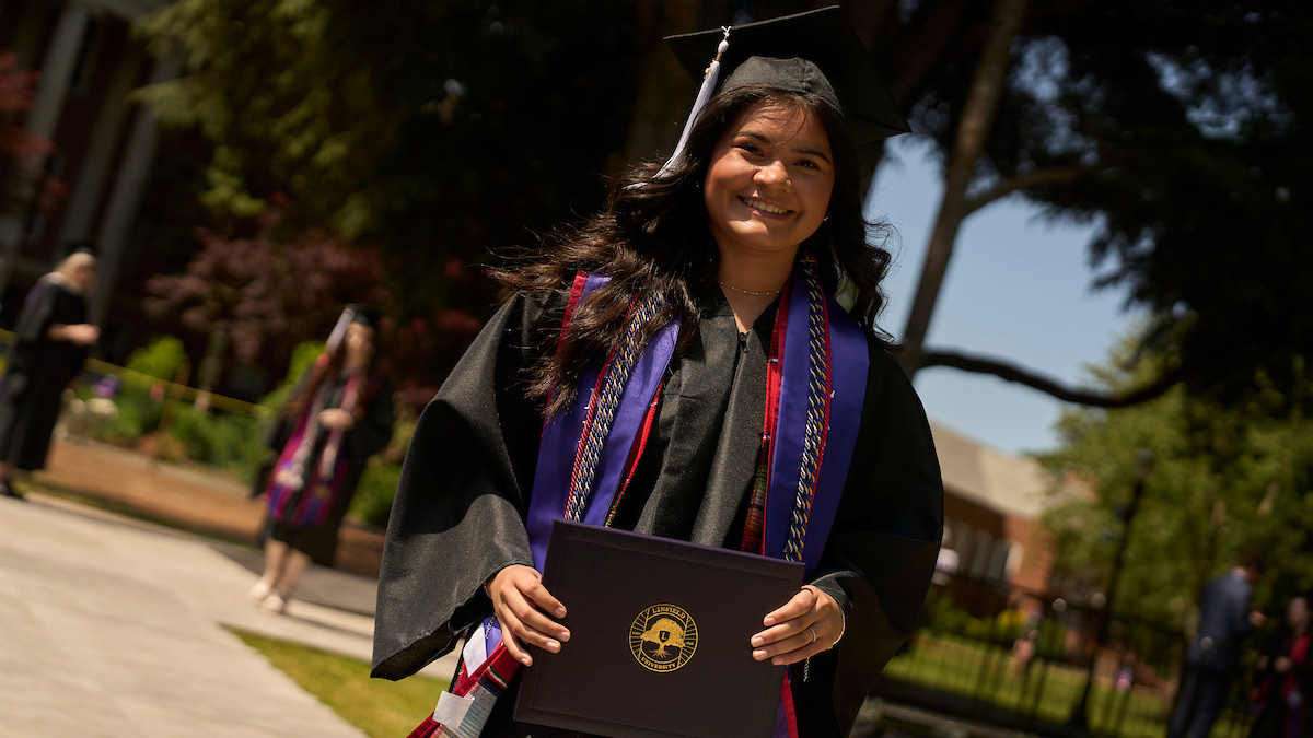 A graduate in cap and gown smiles with their diploma