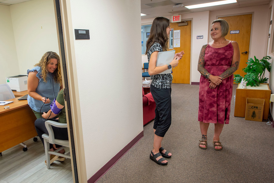 Two student health employees talking and one employee with a student in an exam room.