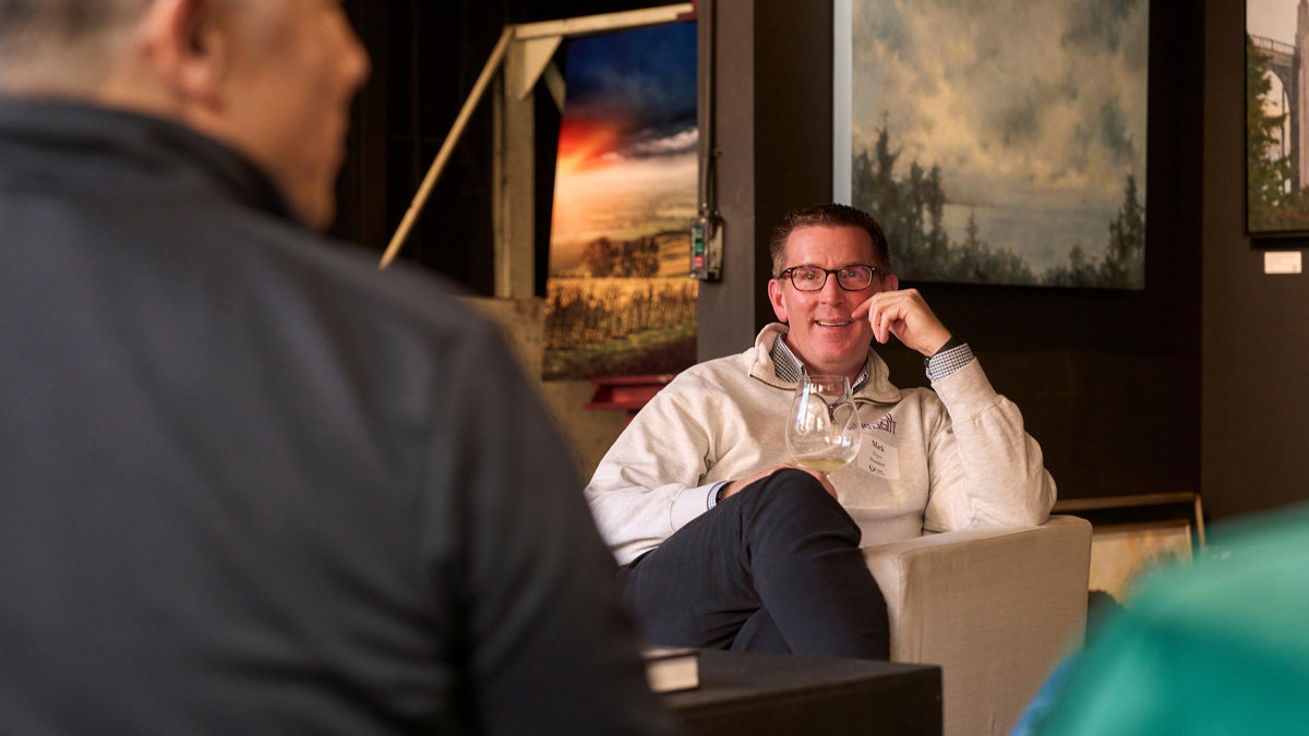 President Mark Blegen sits in a chair actively listening to guests seated in front of camera.