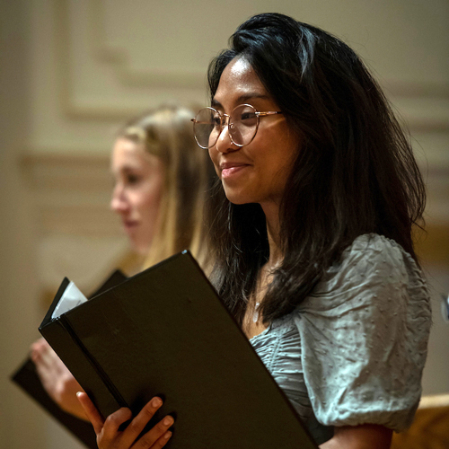 Female student rehearsing in choir, holding music book.