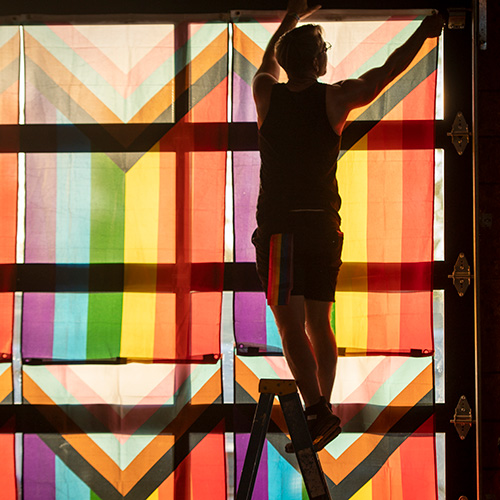 photo of a person hanging pride flags in a window.