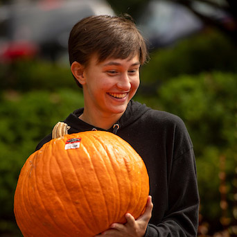 Female student holding a pumpkin during fall festival.