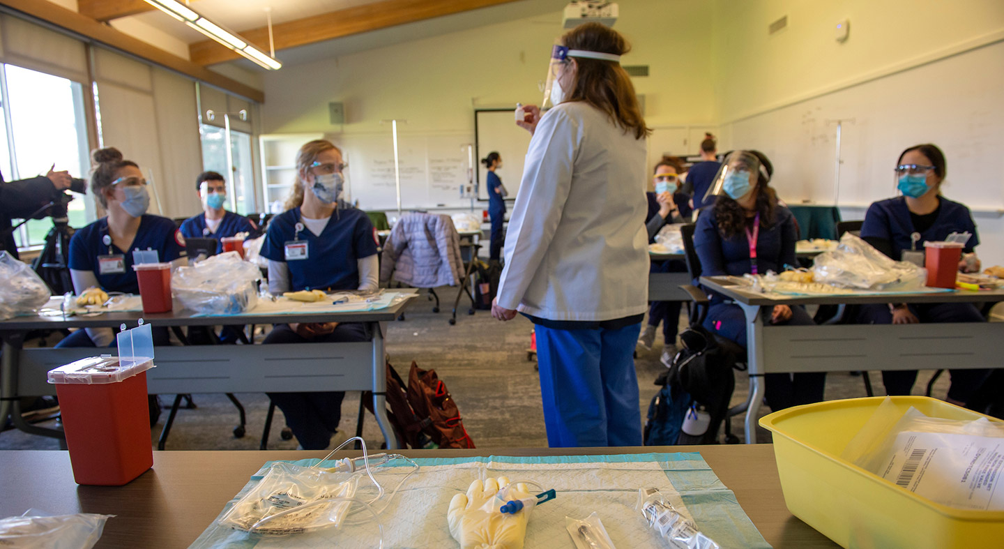 Nursing professor in white lab coat leading classroom of nursing students.