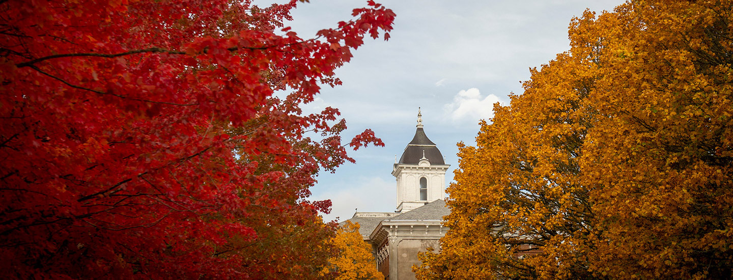 The top of Pioneer Hall through vibrant fall leaves on the trees.