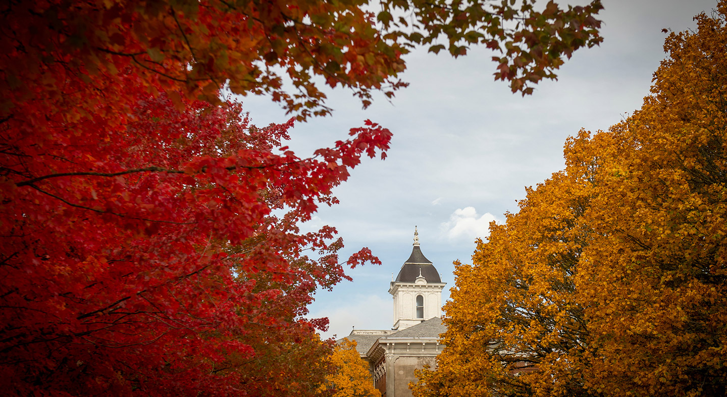 A view of the top of Pioneer Hall through colorful fall leaves on trees in the Oak Grove
