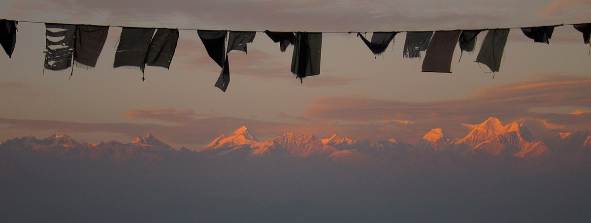 Beautiful purplish-pink sunset over the Himalayas with a string of Buddhist prayer flags in the foreground.