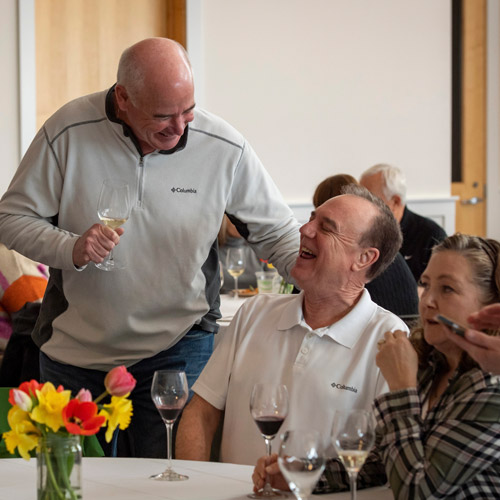 Three Oak & Vine members sitting at a table at a tasting reception enjoying glasses of wine.