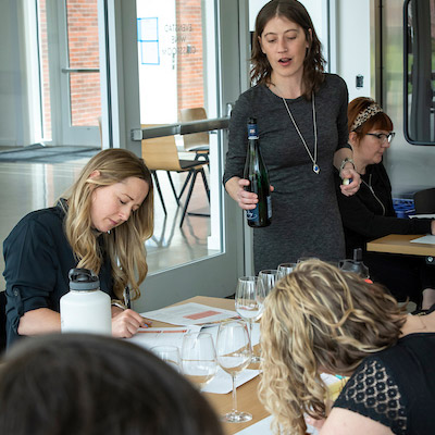 An instructor of WSET Level One talking about a wine with students while pouring in their glasses.