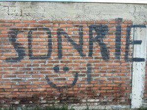 Graffiti on a brick wall saying Sonríe. Smile.