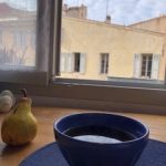 A pear and bowl of tea in front of an open window.