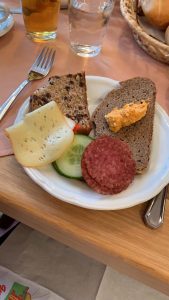 Plate with a traditional Austrian breakfast that includes cheese, sliced meat, and a red pepper-spread on a slice of bread
