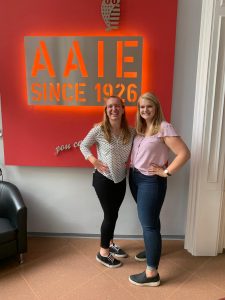 Two people standing in front of a sign that reads: AAIE since 1926