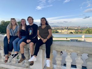 four Linfield students in sitting on a ledge with Schönbrunn in the far background