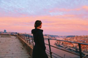 Girl in black jacket with hair tied back overlooks the river and town at sunset