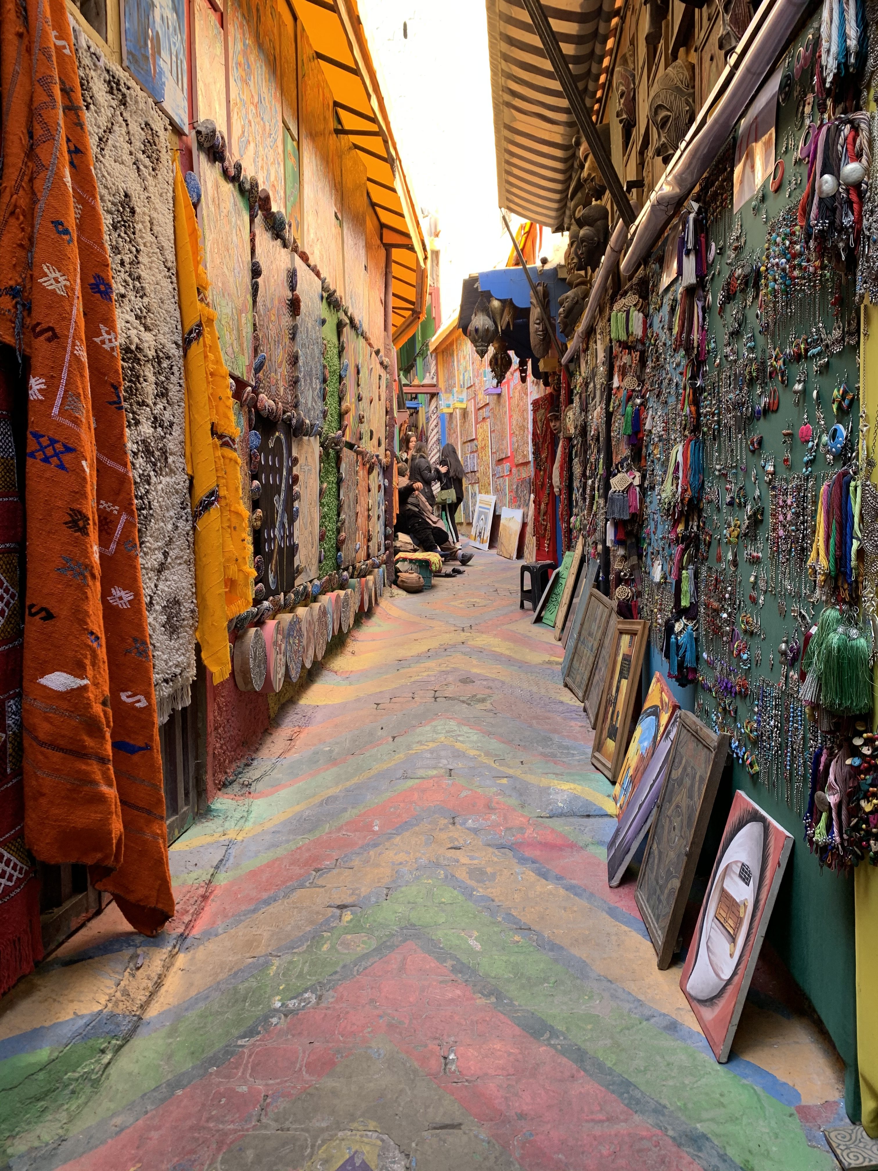 Rainbow street of art - paintings, rugs and many other types of artwork hanging on both sides of the street.