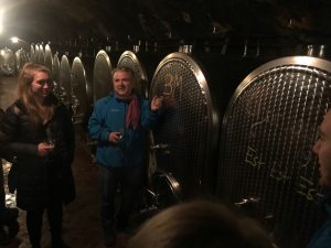 Hermann stands near a wine barrel while Kara stands and listens next to him