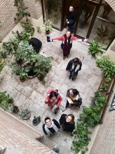 The photo looks down into a courtyard where students are looking up to the camera and standing among plants.