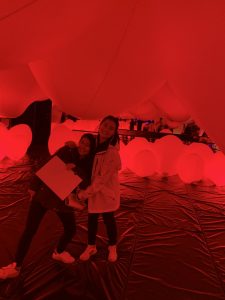 Two girls in a room with very red balloons. 