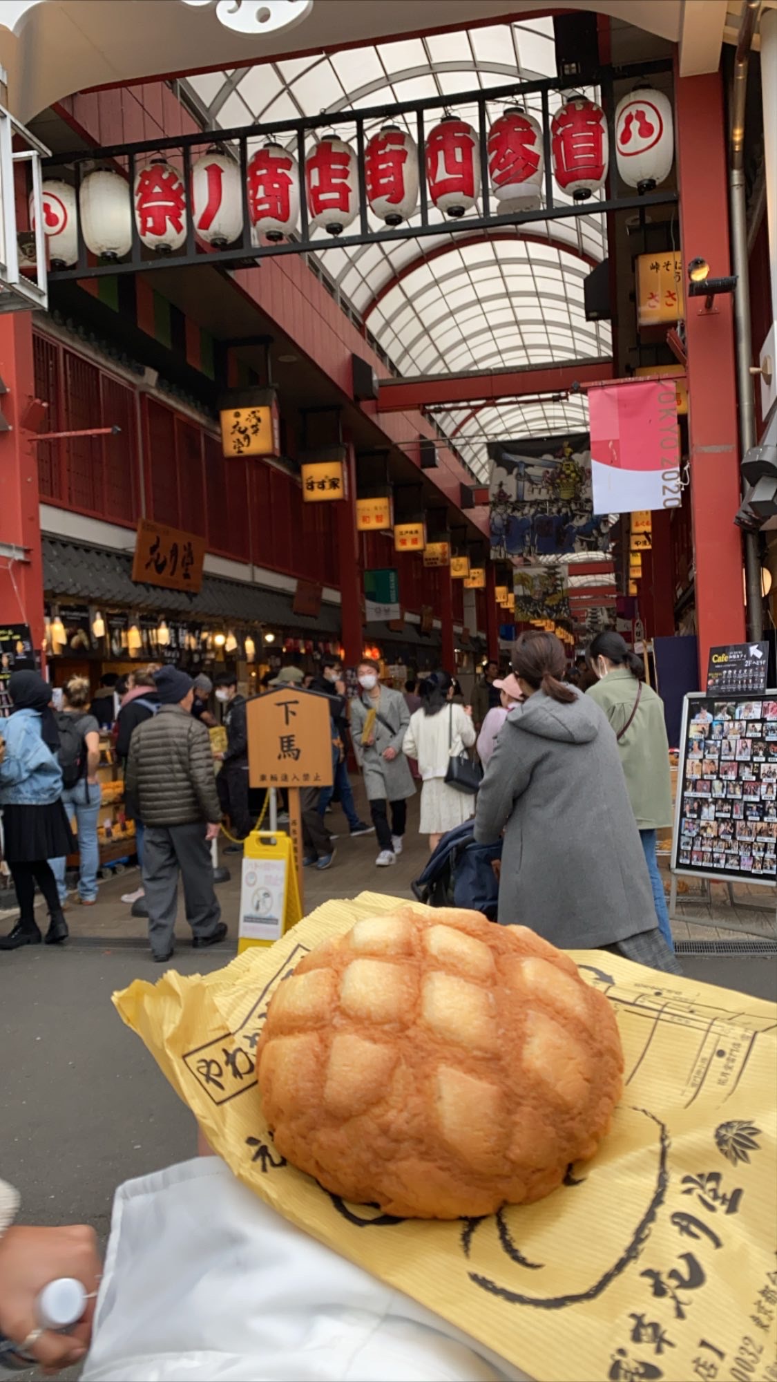 Melon pan being held up in front of a road full of shops and food places