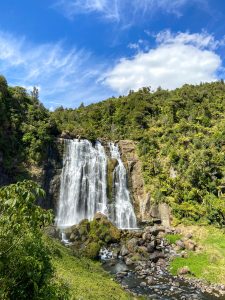 A waterfall with greenery on the sides and a blue sky above