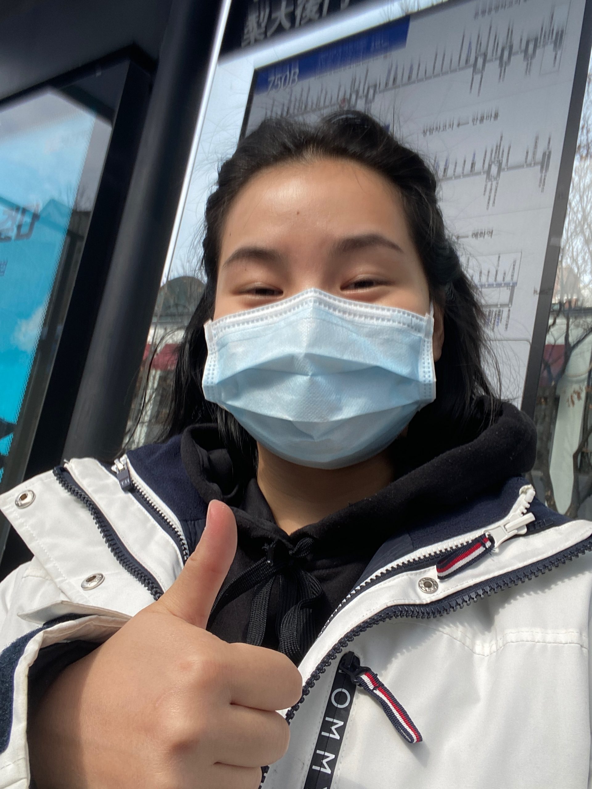 Me showing a thumbs up outside a bus stop, wearing a mask.