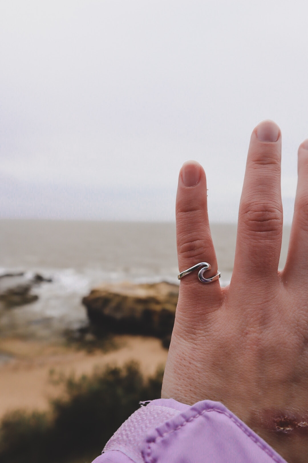 Girls hand wearing a ring with the ocean and rocks in the background.