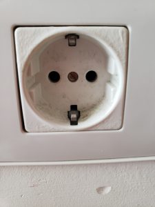 A European electrical outlet with two holes. Pictured on a white wall. 