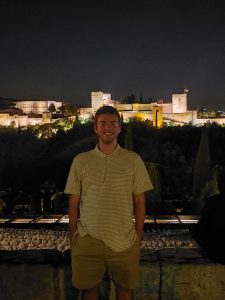 The author wearing a beige shirt and pants in front of the illuminated Alhambra during nighttime.