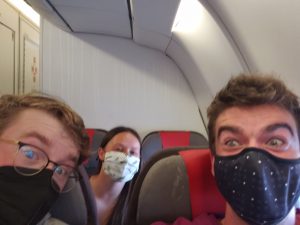 The author and his travel companions minutes after boarding their plane to New York. They are all wearing masks with expressions of exhaustion.