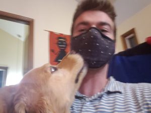 The author, wearing a black mask, receiving kisses from his golden retriever at home. 