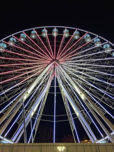 A from-below picture of a ferris wheel lit up in blue and pink.