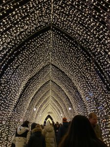 A pointed tunnel of lights with people walking underneath.