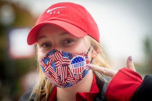 Student points to an I Voted sticker on a flag face mask